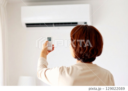 エアコンのリモコンで温度調整をする女性 129022089