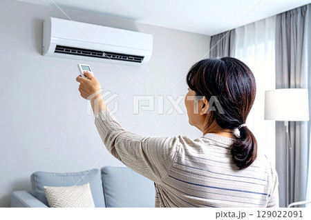 エアコンのリモコンで温度調整をする女性 129022091