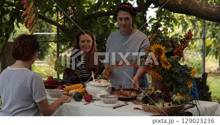 Group of friends celebrate Thanksgiving in a beautiful garden filled with autumn colors and freshly prepared dishes. Decorated table showcases seasonal produce and floral arrangements. 129023236