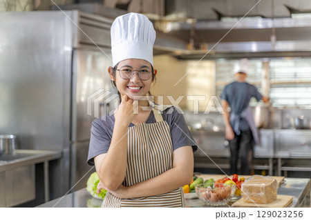 Young Female Chef Smiling in Professional Kitchen with Arms Crossed Young Female Chef Smiling in Professional Kitchen with Arms Crossed 129023256