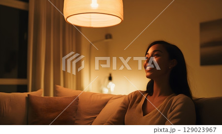 woman relaxing on sofa at night under warm lamplight 129023967