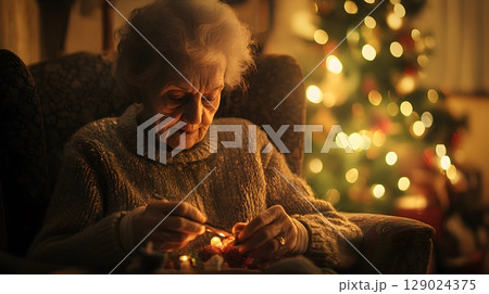 elderly woman knitting by christmas tree 129024375