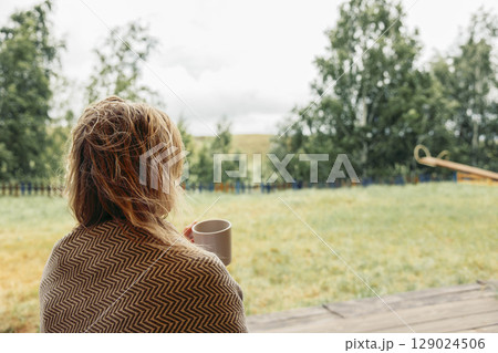 woman drinking warm beverage while looking into distance, rainy outdoor background with natural greens, concept of comfort, calm morning, wellness woman drinking warm beverage while looking into distance, rainy outdoor background with natural greens, concept of comfort, calm morning, wellness 129024506