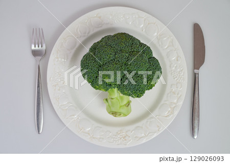 Raw broccoli on white plate with fork and knife 129026093