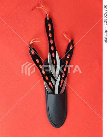 Set of several throwing knives in a case for combat training and sport throwing on a red background. 129026330