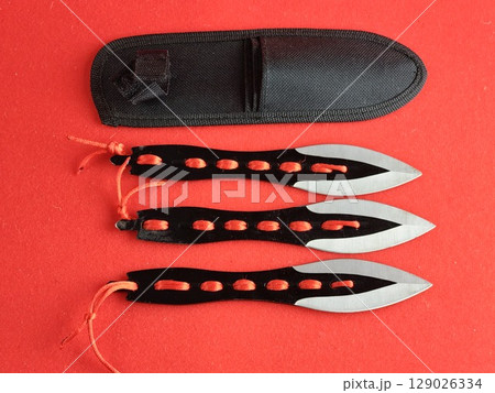Case and three throwing knives for combat training and sport throwing on a red background. Case and three throwing knives for combat training and sport throwing on a red background. 129026334