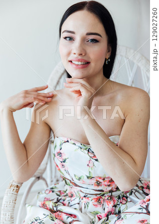 Fashionable woman in summer dress with flowers sitting by window portrait Fashionable woman in summer dress with flowers sitting by window portrait 129027260