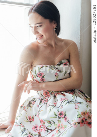 Fashionable woman in summer dress with flowers sitting by window portrait 129027261