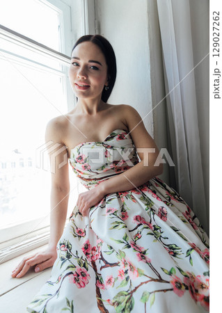 Fashionable woman in summer dress with flowers sitting by window portrait 129027262