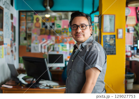 Confident latin man in colorful office, working on computer. Happy, smiling entrepreneur embodies success. Busy, vibrant workspace 129027753