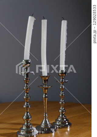 Elegant Collection of Three Silver Candlesticks with Long, White, Dripping Candles Set Against a Soft Gray Wall, Perfect for Creating a Cozy Atmosphere in Any Room or Event Elegant Collection of Three Silver Candlesticks with Long, White, Dripping Candles Set Against a Soft Gray Wall, Perfect for Creating a Cozy Atmosphere in Any Room or Event 129028533