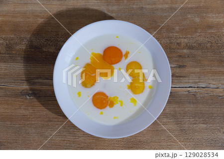 A Delicious Display of Fresh Egg Yolks and Cream Blended Together in a White Bowl Arranged on a Rustic Wooden Table for a Culinary Presentation, Perfect for Breakfast or Baking. A Delicious Display of Fresh Egg Yolks and Cream Blended Together in a White Bowl Arranged on a Rustic Wooden Table for a Culinary Presentation, Perfect for Breakfast or Baking. 129028534