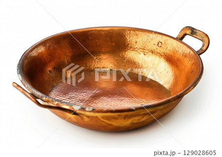 Old and dented copper pan with two handles is standing on a white background 129028605