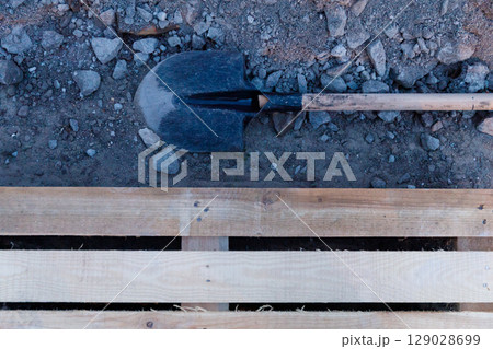 A Classic Spade Resting on Earth with Rocks and Wooden Pallet: Symbol of Hard Work and Construction Efforts A Classic Spade Resting on Earth with Rocks and Wooden Pallet: Symbol of Hard Work and Construction Efforts 129028699