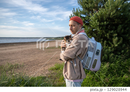 Loving man cuddling petting cat, look at sea coastline, backpack carrier for animal travel comfort 129028944