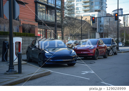 Modern electric cars charging batteries at tesla charging station in modern city environment 129028999