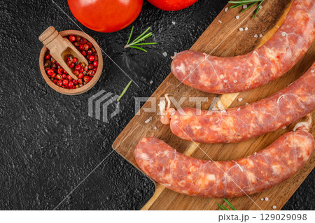 Raw pork sausages with visible fat marbling lie on a wooden board next to coarse salt, red peppercorns, and ripe tomatoes Raw pork sausages with visible fat marbling lie on a wooden board next to coarse salt, red peppercorns, and ripe tomatoes 129029098