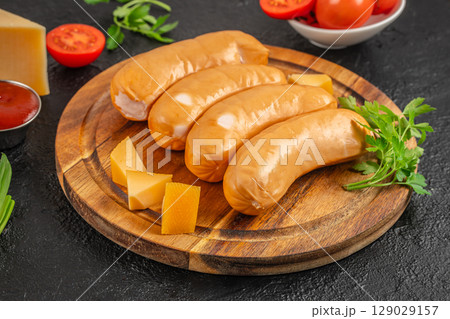 Four smoked sausages with cheese cubes and parsley served on a rustic wooden board with fresh ingredients in the background Four smoked sausages with cheese cubes and parsley served on a rustic wooden board with fresh ingredients in the background 129029157