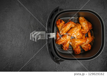 Top view of crispy golden chicken wings freshly cooked in an air fryer basket on a dark textured background. top view. copy space Top view of crispy golden chicken wings freshly cooked in an air fryer basket on a dark textured background. top view. copy space 129029162