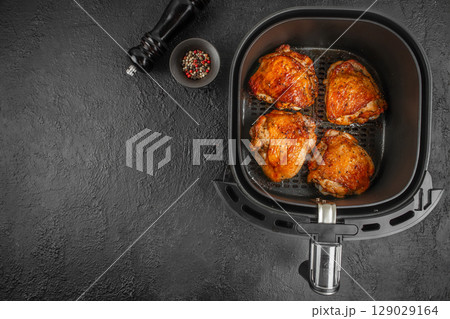 Roasted chicken thighs cooked in an air fryer basket with pepper mix and grinder on a dark textured background. top view. copy space Roasted chicken thighs cooked in an air fryer basket with pepper mix and grinder on a dark textured background. top view. copy space 129029164