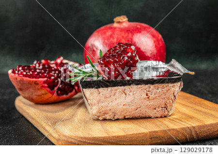 Liver pate with a pomegranate jelly topping in a foil container, garnished with fresh rosemary and served alongside whole and halved pomegranates 129029178