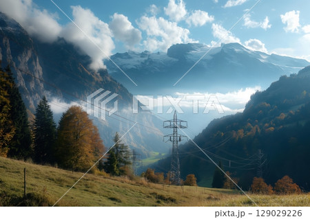Scenic landscape featuring a high voltage transmission line crossing a lush green mountain valley on a bright sunny day, with clouds casting shadows on the distant peaks 129029226