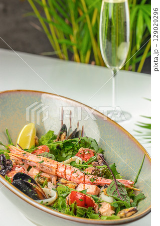 A vibrant seafood salad with shrimp, mussels, and fresh greens is served in a rustic bowl alongside a refreshing glass of sparkling wine A vibrant seafood salad with shrimp, mussels, and fresh greens is served in a rustic bowl alongside a refreshing glass of sparkling wine 129029296