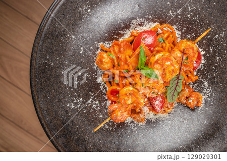 Spaghetti with shrimp in vibrant tomato sauce is garnished with fresh herbs and grated cheese for a flavorful seafood pasta dish 129029301