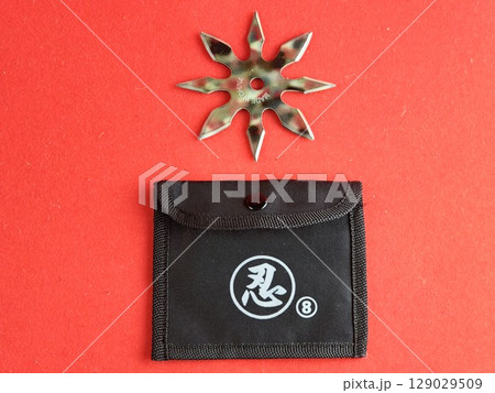 A star-shaped shuriken painted in military colors with a sheath on a red background. The inscription on the shuriken says Made in China. 129029509