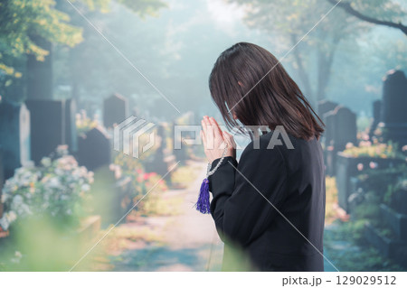 喪服を着て墓地で手を合わせる女性 129029512