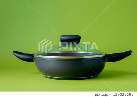 Modern black skillet with a glass lid is standing on a green background 129029599