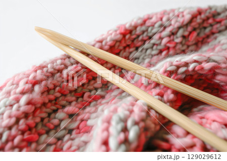 Bamboo knitting needles with pink end cap resting on pink and grey wool, embodying the craft of knitting and handiwork 129029612