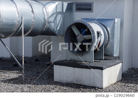 Detailed View of Industrial Ventilation System Featuring Metal Ducts and Exhaust Fan with Blades Positioned for Efficient Airflow on Building's Exterior Surface 129029660