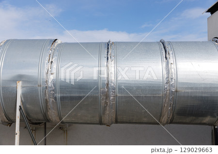 Shiny Metal Ducting Installed on the Exterior of a Building with Brilliant Blue Sky in the Background Providing a Modern Industrial Vibe and Strong Aesthetic Appeal 129029663