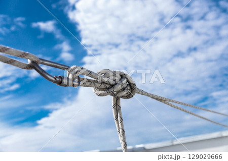 Close-Up View of a Knotted Rope Secured with a Carabiner Against a Bright Blue Sky Filled with Fluffy White Clouds, Showcasing Outdoor Adventure and Climbing Equipment 129029666