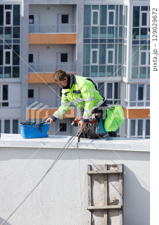 Construction Worker Painting a Building Roof: Attention to Safety and Precision in Urban Renovation Construction Worker Painting a Building Roof: Attention to Safety and Precision in Urban Renovation 129029672