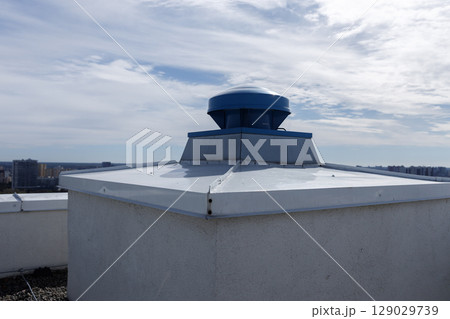 A Close-Up Look at a Rooftop Ventilation System with Blue Fan on Flat Roof Surrounded by Urban Skyline under Clear Sky A Close-Up Look at a Rooftop Ventilation System with Blue Fan on Flat Roof Surrounded by Urban Skyline under Clear Sky 129029739