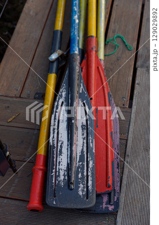 Colorful Collection of Used Paddles Resting on a Wooden Deck Background Evoking Memories of Adventurous Water Activities and Outdoor Fun in Natural Settings 129029892