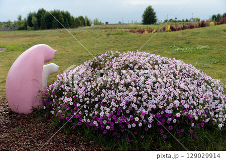 Whimsical Garden Sculpture Surrounded by Colorful Petunias: A Serene Moment Captured in Nature with Pink and Purple Blooms Enhancing the Playful Atmosphere of the Outdoors 129029914