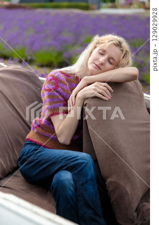A Serene Moment: A Young Woman with Blonde Hair Relaxing on a Sofa in a Lavender Field, Capturing Tranquility and Comfort in a Beautiful Nature Setting 129029928