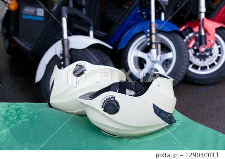 Two White Helmets Resting on a Green Surface Amidst Colorful Scooters and Motorcycles in a Vivid Outdoor Setting Two White Helmets Resting on a Green Surface Amidst Colorful Scooters and Motorcycles in a Vivid Outdoor Setting 129030011