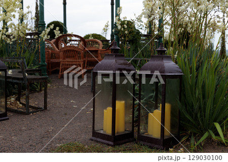 Charming Outdoor Setting with Lanterns and Rustic Furniture Surrounded by Lush Greenery and White Flowers, Creating a Cozy Atmosphere for Relaxation and Gathering 129030100