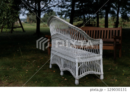 Elegant and Inviting White Wicker Chair Accompanied by a Rustic Brown Bench Amidst a Lush Green Outdoor Setting Perfect for Relaxation and Leisure Activities in Nature Elegant and Inviting White Wicker Chair Accompanied by a Rustic Brown Bench Amidst a Lush Green Outdoor Setting Perfect for Relaxation and Leisure Activities in Nature 129030131