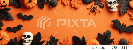 Halloween themed background with copy space and frame of spooky decorations including pumpkins, skulls, bats, and leaves on orange backdrop 129030335