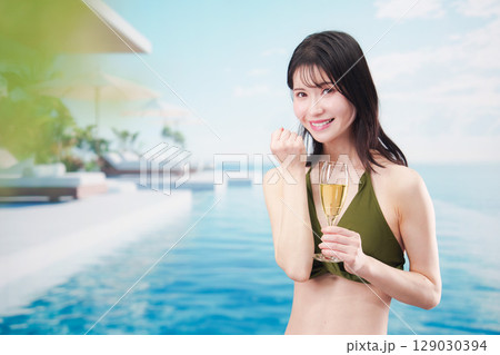 リゾートのプールで水着を着てスパークリングワインを飲む若い女性 129030394