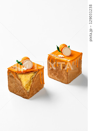 Two cubic mango cakes with orange icing dripping on white background Two cubic mango cakes with orange icing dripping on white background 129031238