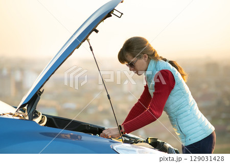 Young woman standing near broken down car with popped up hood having trouble with her vehicle. Young woman standing near broken down car with popped up hood having trouble with her vehicle. 129031428