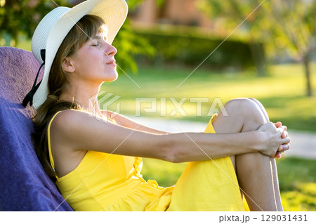 Young woman relaxing outdoors on sunny summer day. Happy lady lying down on comfortable beach chair daydreaming thinking. Calm beautiful smiling girl enjoying fresh air relaxing with closed eyes. Young woman relaxing outdoors on sunny summer day. Happy lady lying down on comfortable beach chair daydreaming thinking. Calm beautiful smiling girl enjoying fresh air relaxing with closed eyes. 129031431