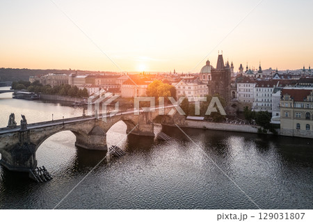 A breathtaking sunrise casts warm light over the historic Charles Bridge in Prague, illuminating the Vltava River and the charming old town buildings on the banks. 129031807