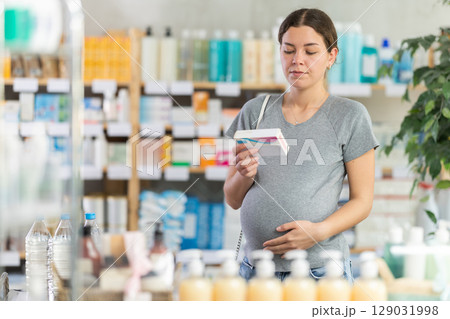 Portrait of attentive pregnant woman holding and choosing box with best pills to improve well-being in pharmacy Portrait of attentive pregnant woman holding and choosing box with best pills to improve well-being in pharmacy 129031998